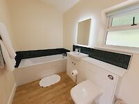 Sleek bathroom showing Bath tub, Sink, Toilet, heated towel rail, mirror and underfloor heating.